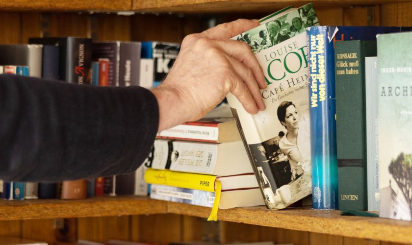 Das Foto zeigt eine Hand, die ein Buch aus einem Offenen Bücherregal entnimmt